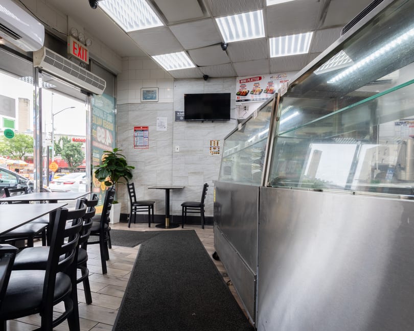 Interior of a restaurant with black tables and chairs, a display case, and an exit sign.