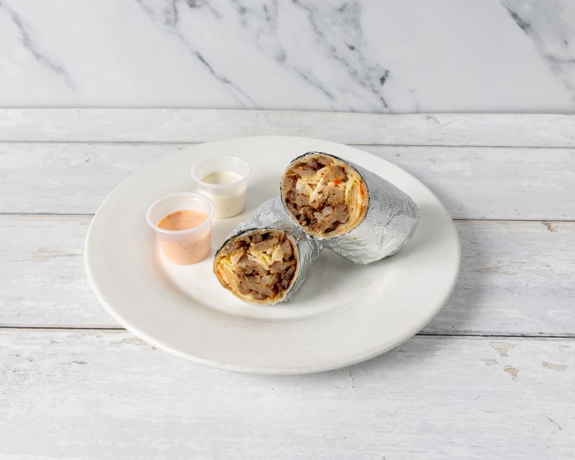 Two foil-wrapped shawarma wraps with meat and vegetables, served with two dipping sauces on a white plate.
