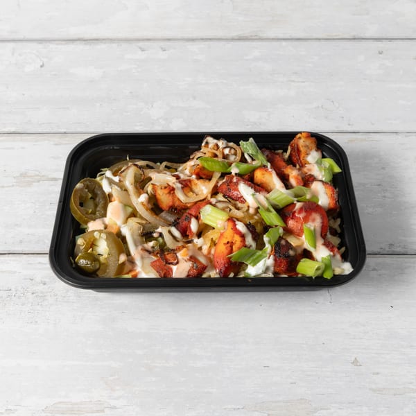 A black takeout container filled with chicken, rice, onions, jalapeños, and sauces.