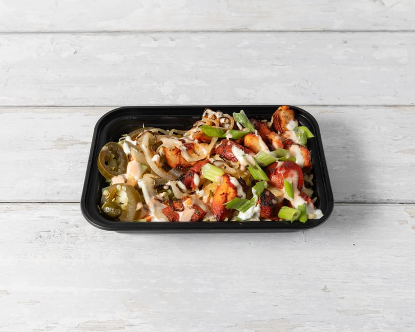A black takeout container filled with chicken, rice, onions, jalapeños, and sauces.