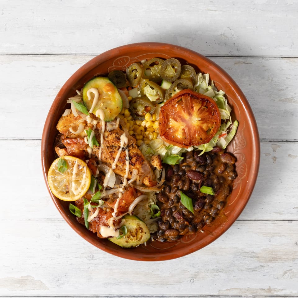 Overhead view of a colorful chicken and black bean bowl with grilled vegetables and lemon.