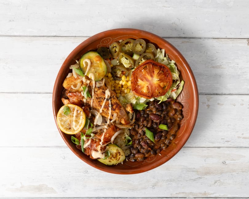 Overhead view of a colorful chicken and black bean bowl with grilled vegetables and lemon.