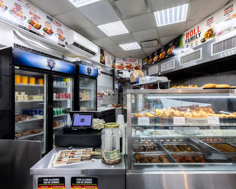 A brightly lit counter inside a restaurant, displaying food in a glass case and menu boards above.