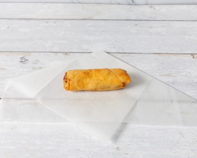 A single golden-brown egg roll rests on a white paper liner against a distressed white wooden background.