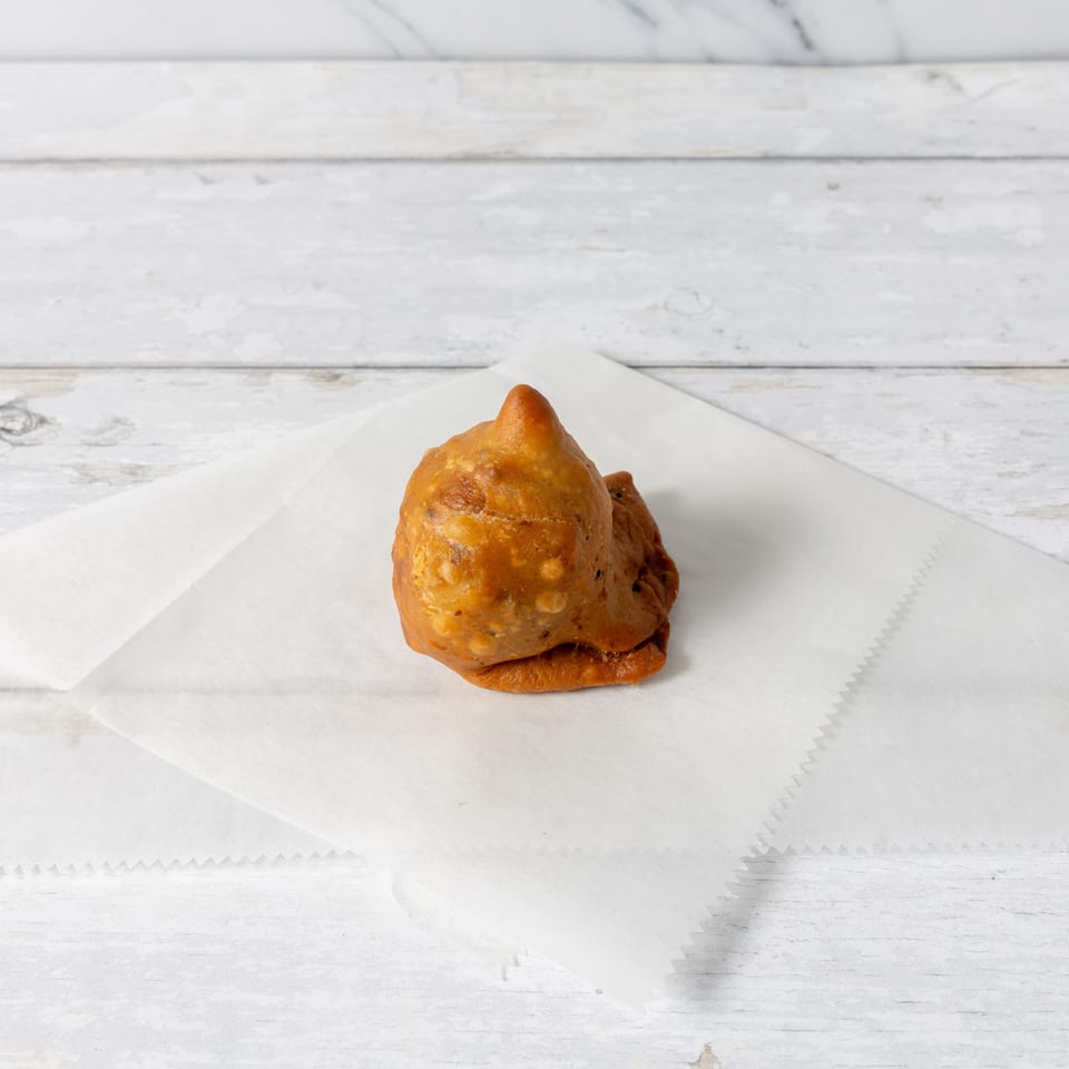 A single golden-brown samosa rests on a white paper napkin against a light wooden background.