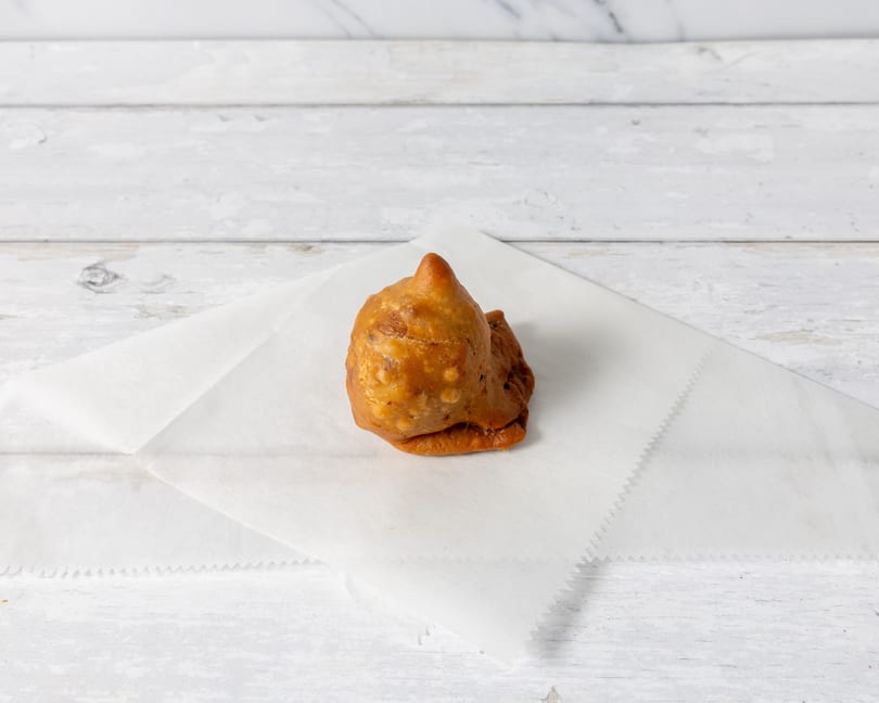 A single golden-brown samosa rests on a white paper napkin against a light wooden background.