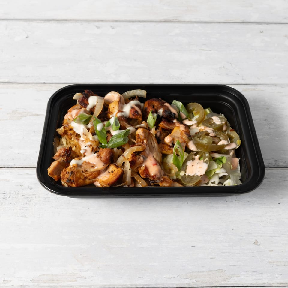 A black takeout container filled with grilled chicken, onions, green onions, and jalapeños, drizzled with sauce.