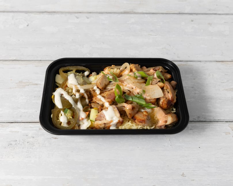 Chicken and rice bowl with jalapeños, onions, and sauces in a black container.