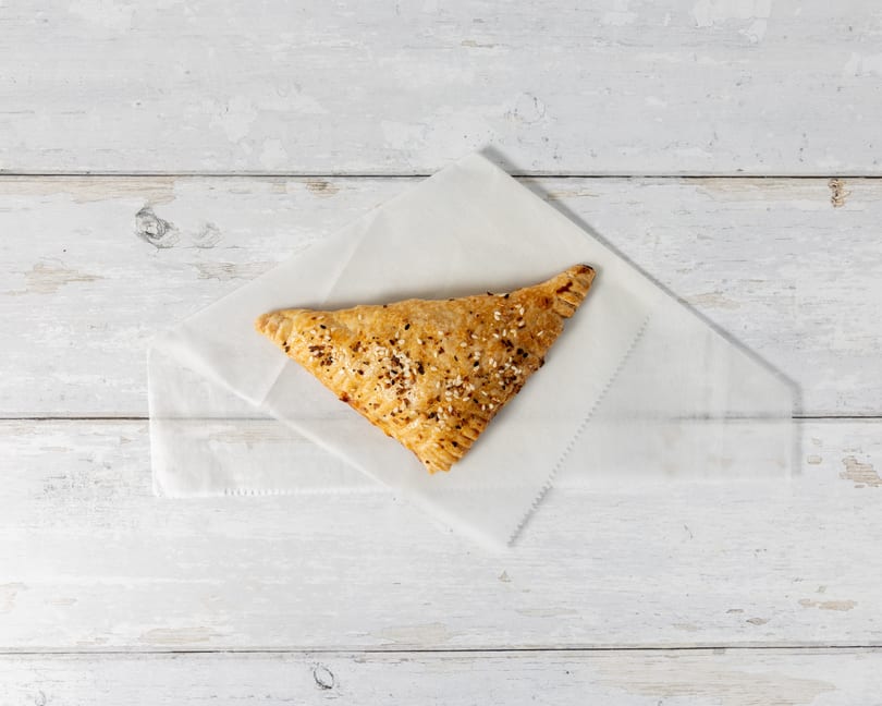 Golden-brown savory pastry with sesame and herb topping on white parchment paper, on a distressed white wooden surface.